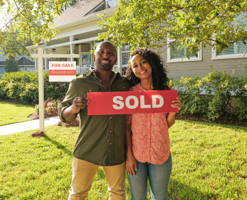 Couple in front of a house holding a sold sign.